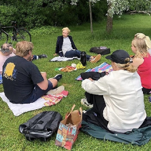 Sex personer som vi ser bakhuvudet på sitter på filtar på en gräsmatta i en park och samtalar med varandra. I mitten ser vi Jonas Frånander.
