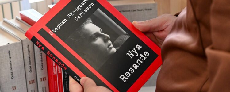 Händer håller boken 'Nya Resande' av Stephan Skougaard Carlsson med rött omslag och svartvitt porträtt, framför en bokhylla.