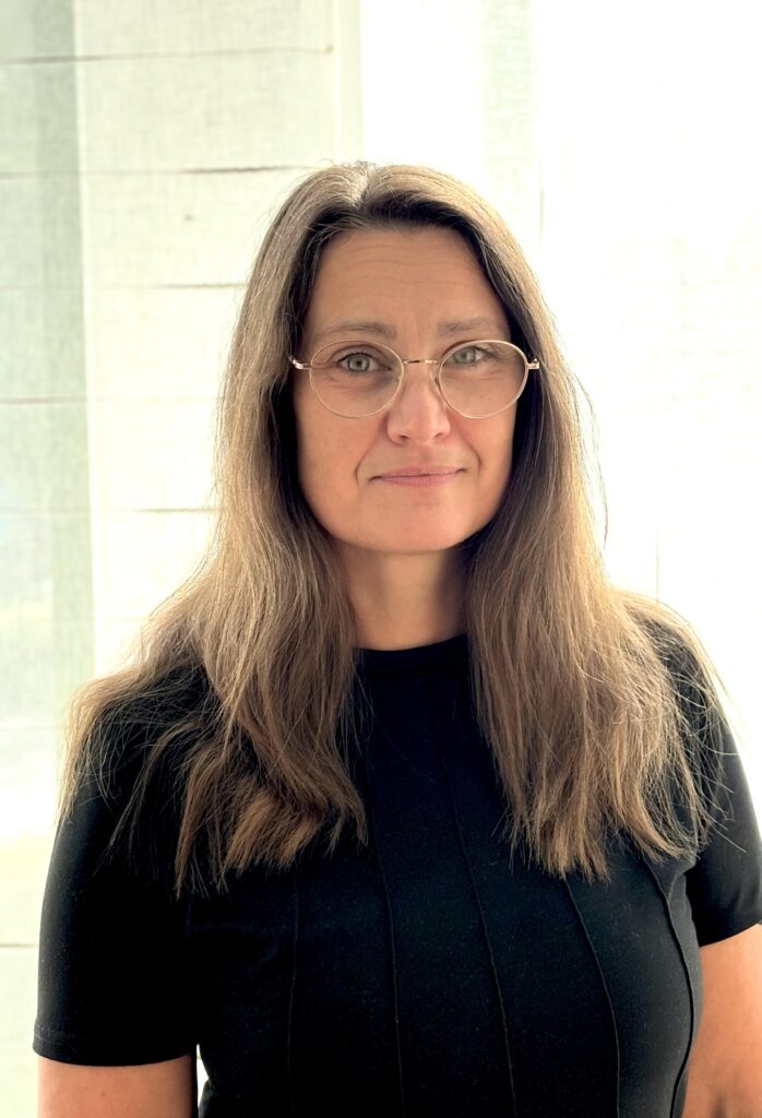 Porträtt av en kvinna med ljusbrunt hår ner över axlarna, svart tröja och glasögon.