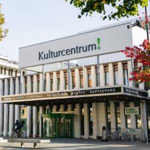 Vit byggnad med stor text på fasaden där det står Kulturcentrum! Ovanför entrén står det texten: Folkbibliotek, konsthall, folkets hus, teater, restaurang. Ett träd med röda löv syns till höger i bild.