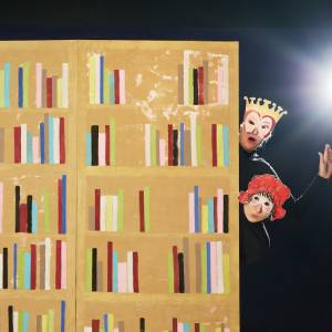 Tre figurer med masker på huvudena tittar fram ifrån en vägg som är målad som en bokhylla. Bakgrunden är svart och figurerna är klädda i svart. Den vänstra figuren har en vargmask, den översta högra har en mask med ögon och krona på huvudet och den nedersta till höger en mask med ögon och röd hatt.