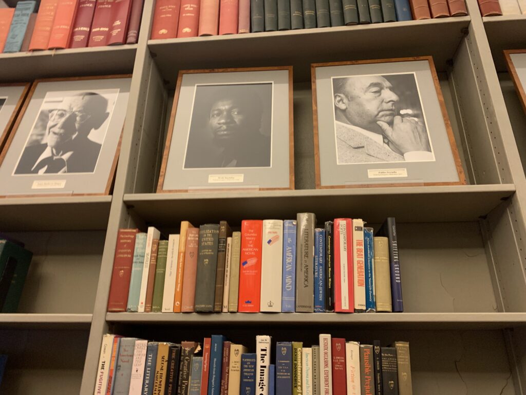 En beskuren bild av en bokhylla med svartvita inramade porträtt på den näst översta raden. 