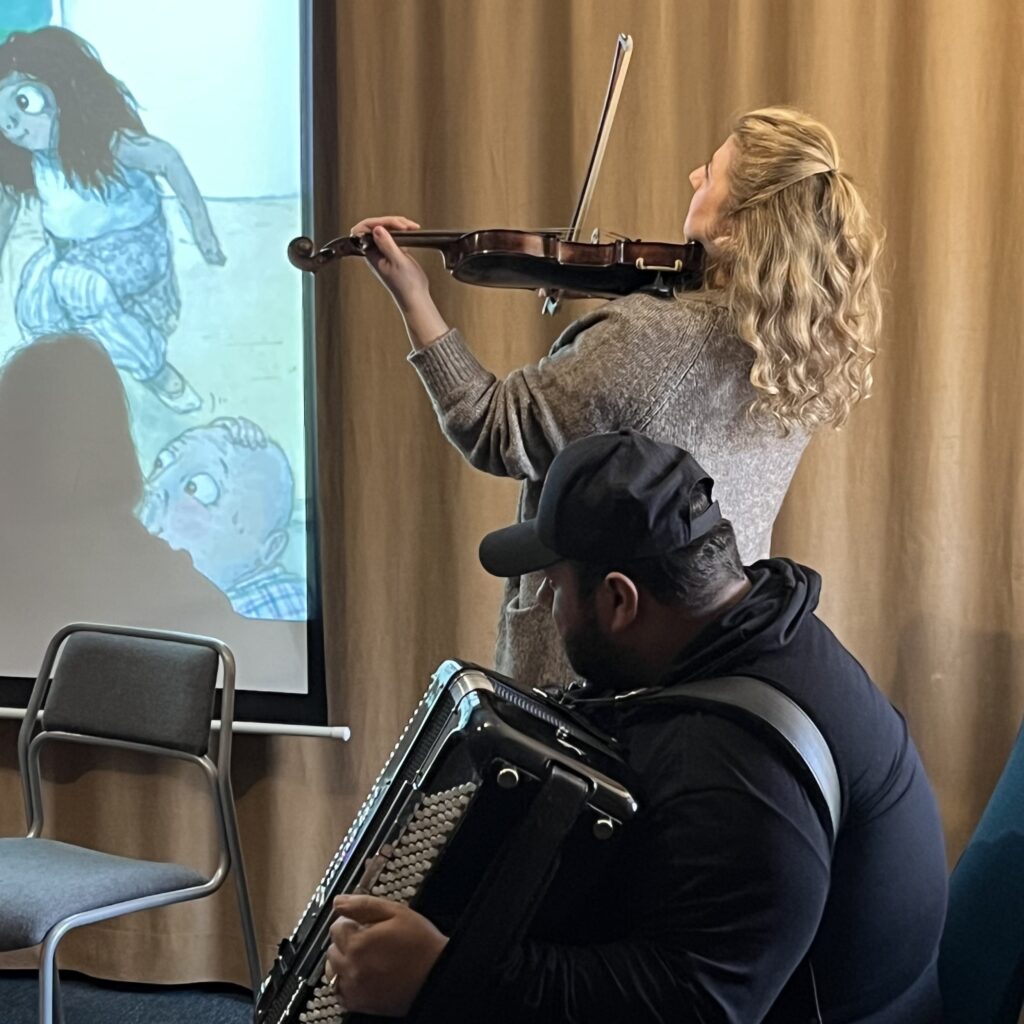 De två musikerna spelar till projicerad barnbok på väggen.