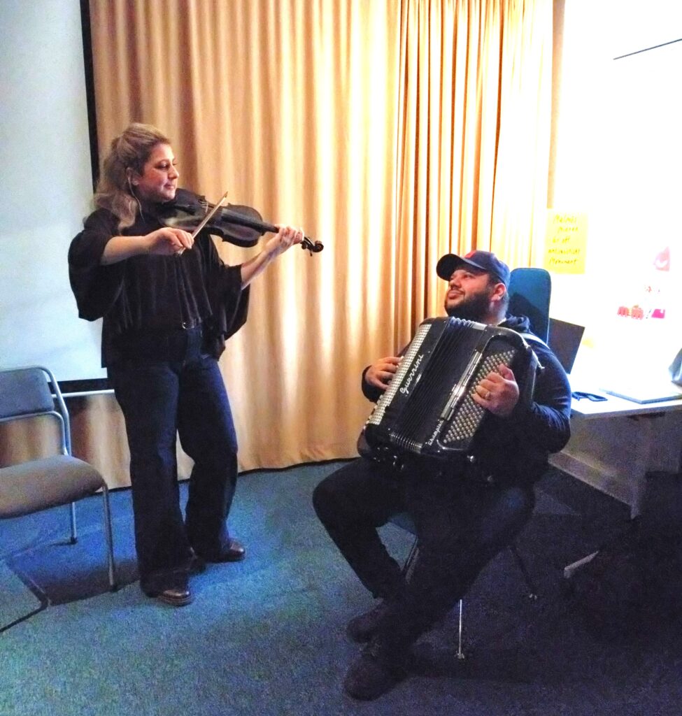 En kvinna står upp och spelar fiol, en man sitter ner och spelar dragspel.