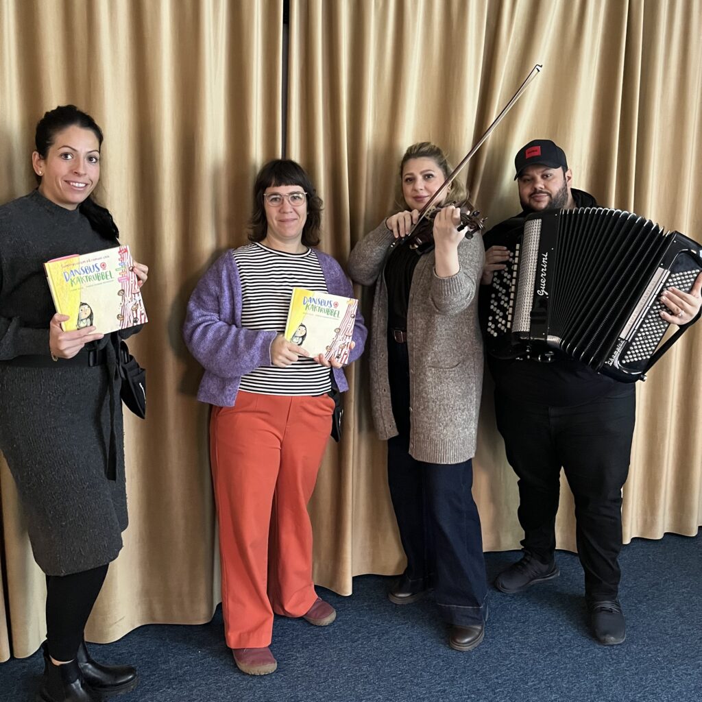 Fyra personer står uppradade, två håller i boken Dansbus och kaktrubbel, en i en fiol och en i ett dragspel.