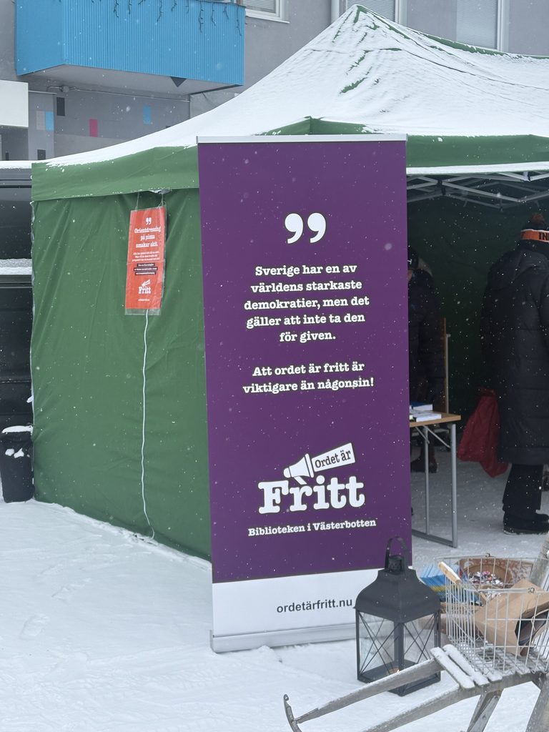Affisch utanför tält på vintermarknad: Sverige har en av världens starkaste demokratier, med det gäller att inte ta den för given. Att ordet är fritt är viktigare än någonsin.