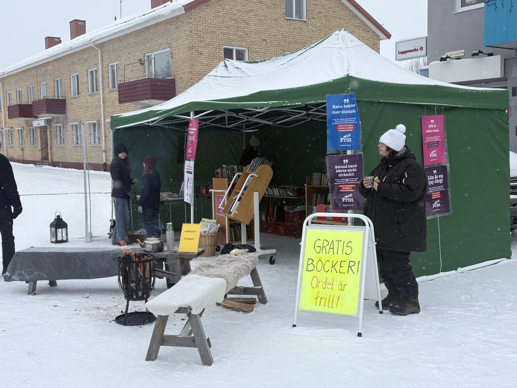 Tält på vintermarknad. Skylt utanför "Gratis böcker, Ordet är fritt!" och affischer från kampanjen.