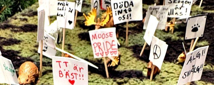 Miniatyrdiorama av en skog där små älgfigurer demonstrerar med handgjorda skyltar på tandpetare, bland annat "Låt skogen va!", "Moose pride" och "Döda inte oss!".